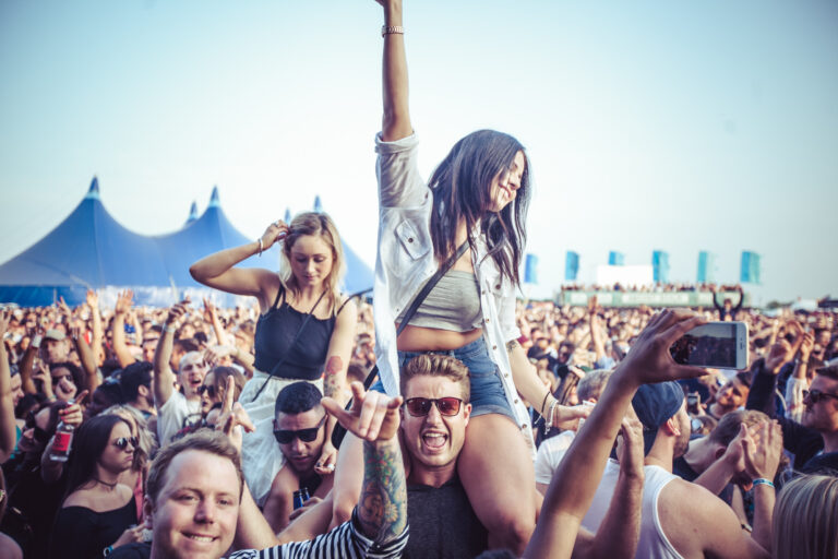 Girl Sitting on Mans Shoulders in Crowd of People at Festival Event