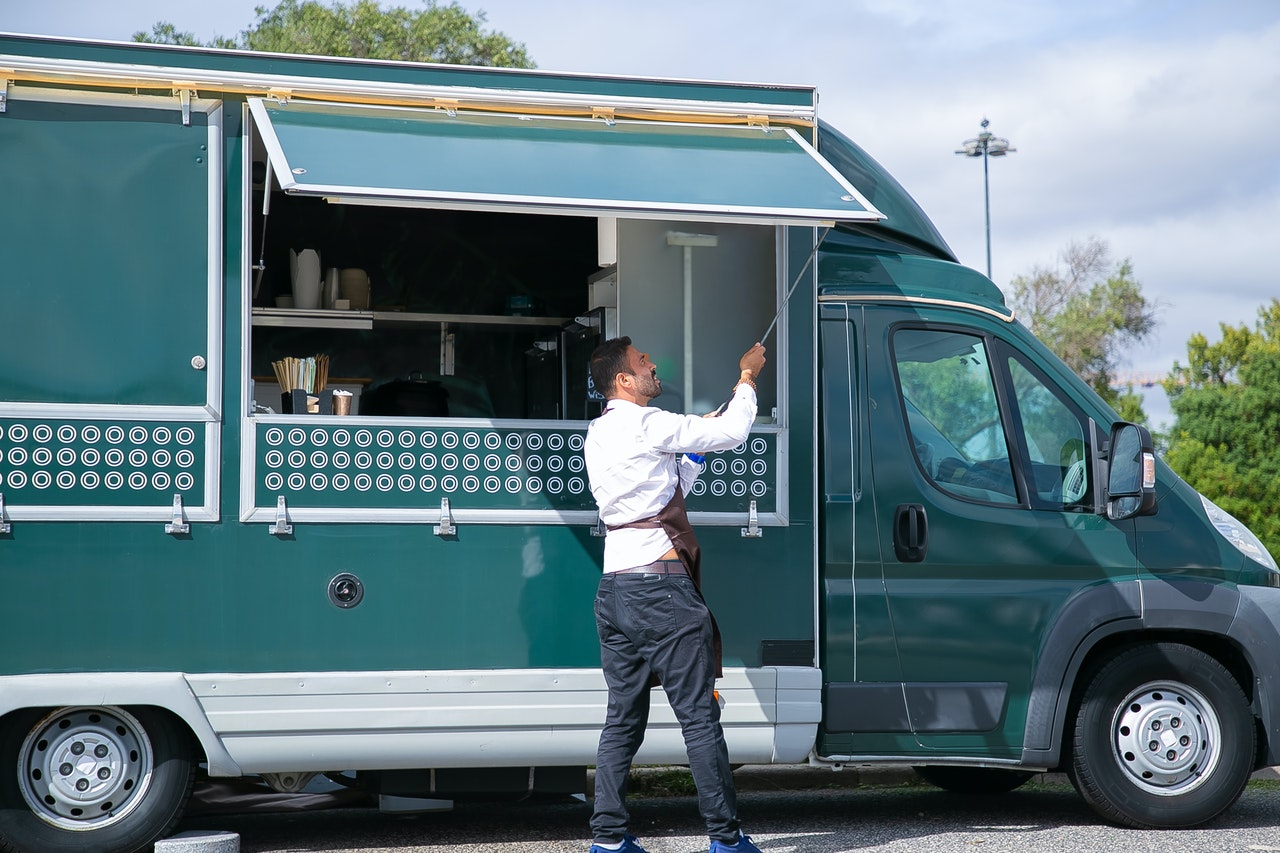 Waiter opening food truck parked in green park